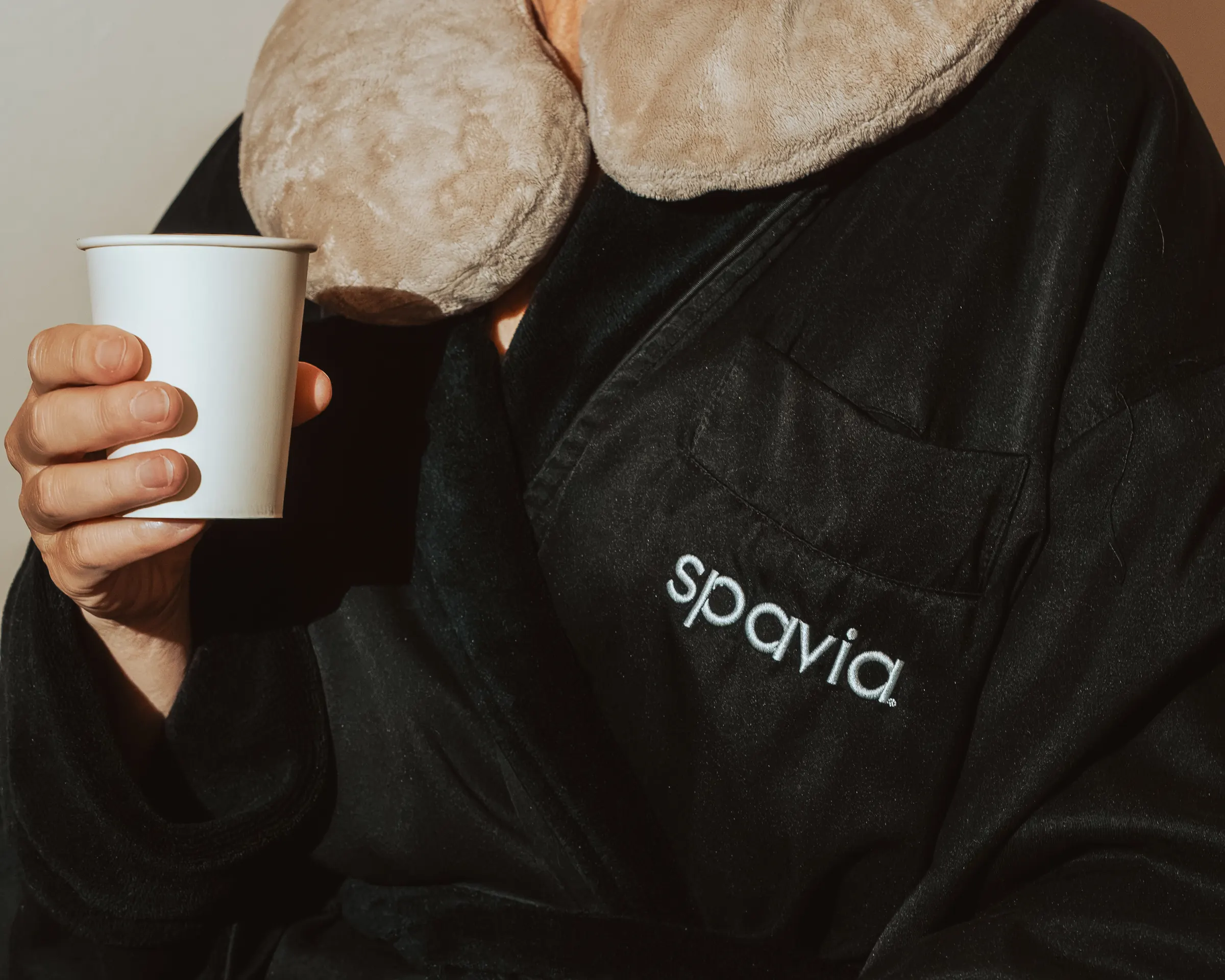 A guest in a Spavia robe holding a warm drink